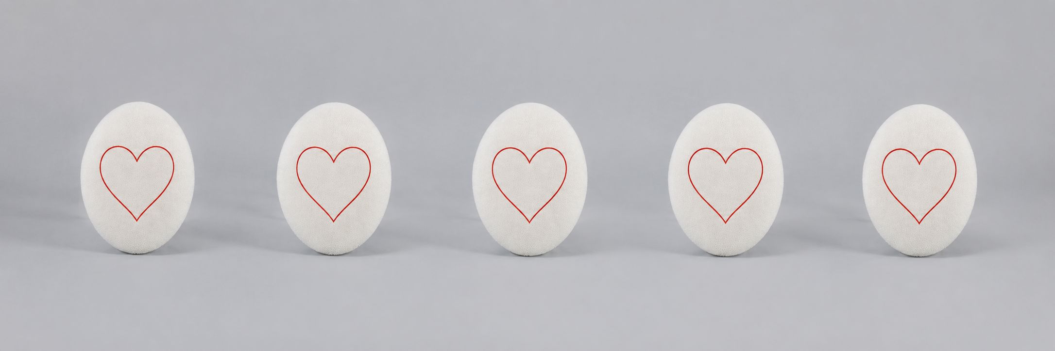 A white oval object with a simple red heart outline drawn in the center, set against a plain gray background.