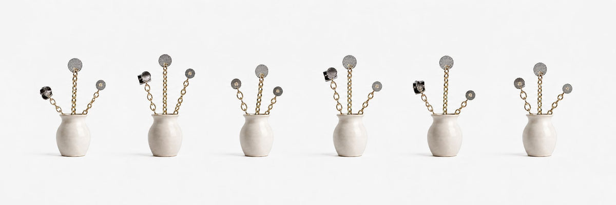 Five identical white vases, each containing gold chain stems topped with circular, metallic, flower-like ornaments, are evenly spaced against a plain white background.
