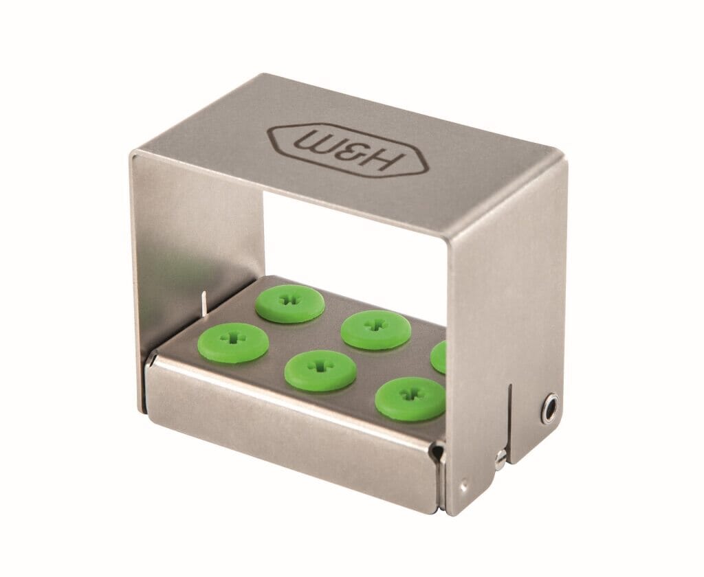 The W&H Piezomed Tip cassette is a rectangular metal holder with an open front and top, featuring six green circular buttons in two rows. The W&H brand indicates its compatibility with Piezomed systems.