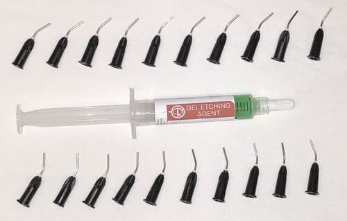 A Cusp-Lok Etchant Gel 37% phosphoric acid 6.5g syringe by Reliance sits on a white surface, encircled by 18 black dispensing tips—perfect for orthodontic bonding and enamel conditioning procedures.