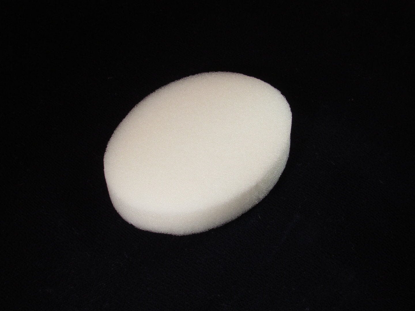 A white, oval-shaped C-Sponge Regular polyurethane surgical throat pack by Xemax is shown on a black surface, photographed with soft lighting. Sold in bags of 100.