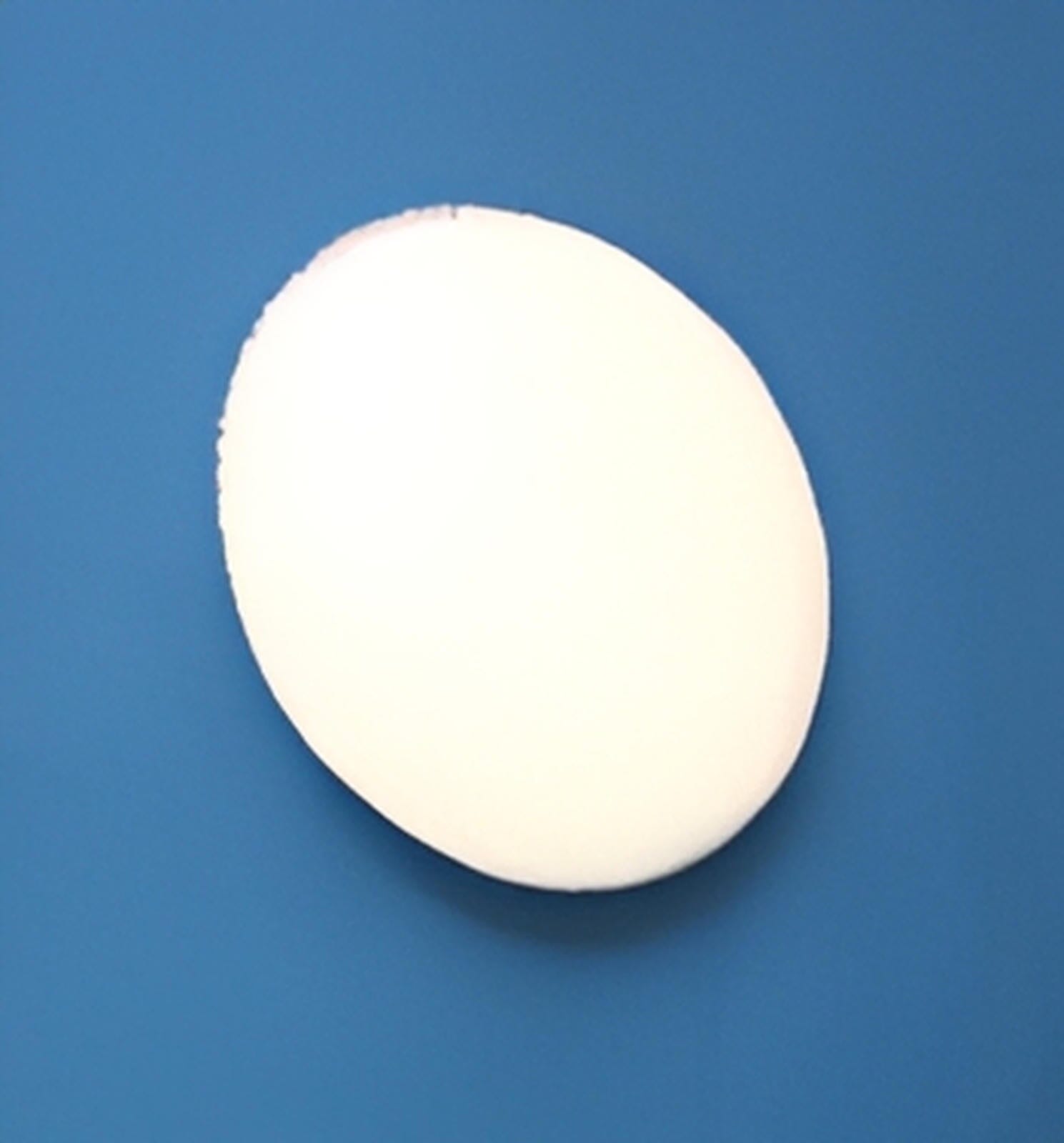 A C-Sponge Pedo - Surgical Throat Pack Pediatric (50/bag), a white, oval-shaped absorbent sponge, is shown resting on a blue textured surface.