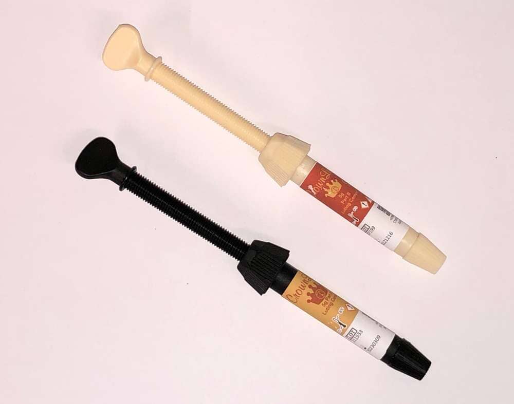 Two Cusp-Lok Self Cure Crown Lok A & B Paste syringes by Xemax Surgical Products Inc. are placed diagonally on a white background, each with a color-coded plunger and a label featuring text and graphics.