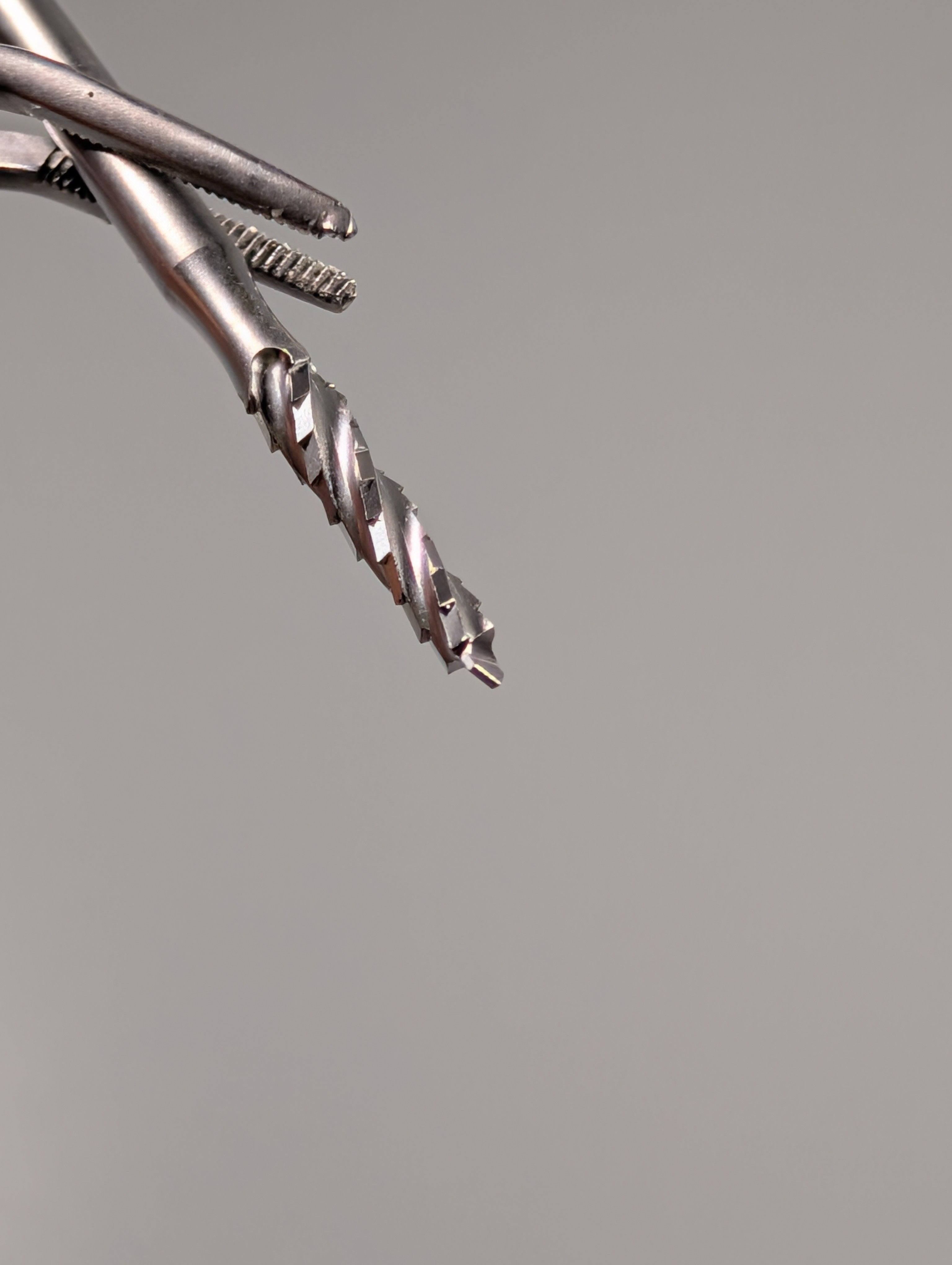 Close-up of three Dentech Lindemann Drill 2.5mm Externally Cooled Stainless Steel Surgical Burs with spiral flutes, arranged diagonally on a grey background, showcasing sharp tips and precise edges for implant site preparation.