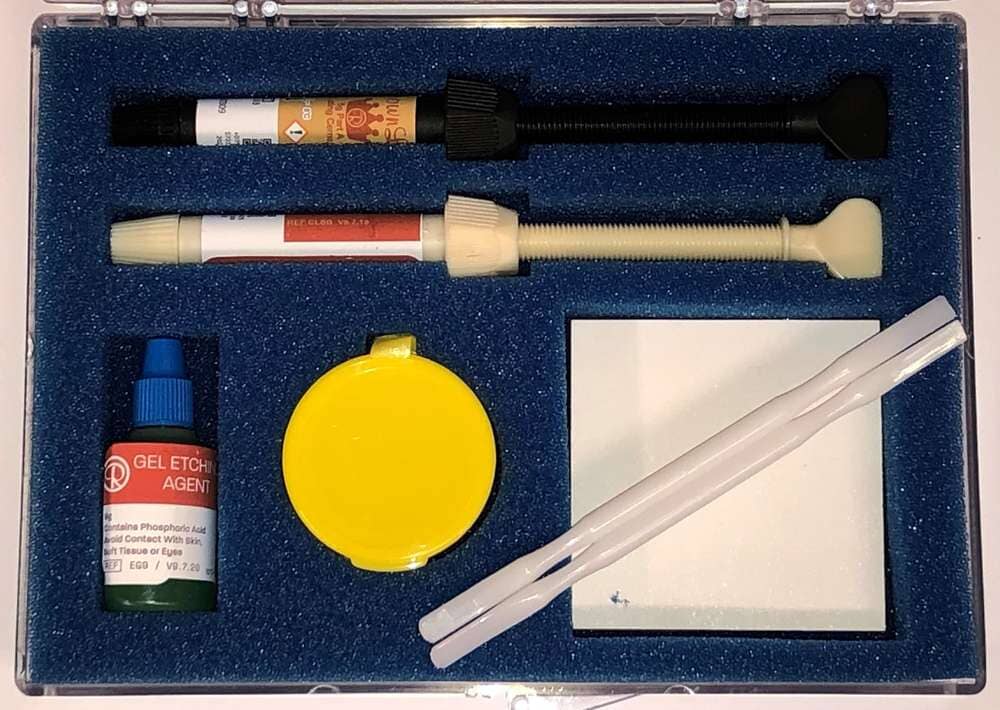 The Xemax Cusp-Lok Self Cure Complete Bonding Convenience Kit includes syringes, gel etch agent bottle, yellow container, white mixing pad, and applicators in a blue foam insert within a clear case—ideal for orthodontic bonding.