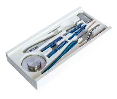 A white tray holds the McBio SuperTack Intro kit with 4 STS, featuring blue and metallic surgical or dental tools such as tweezers, screwdrivers, a cylindrical container, and other small precision instruments.
