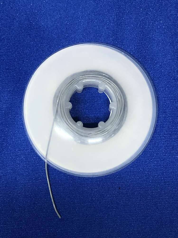 A spool of Dynaflex Orthodontic Elastic Power Thread with a white center is displayed on a bright blue fabric background.