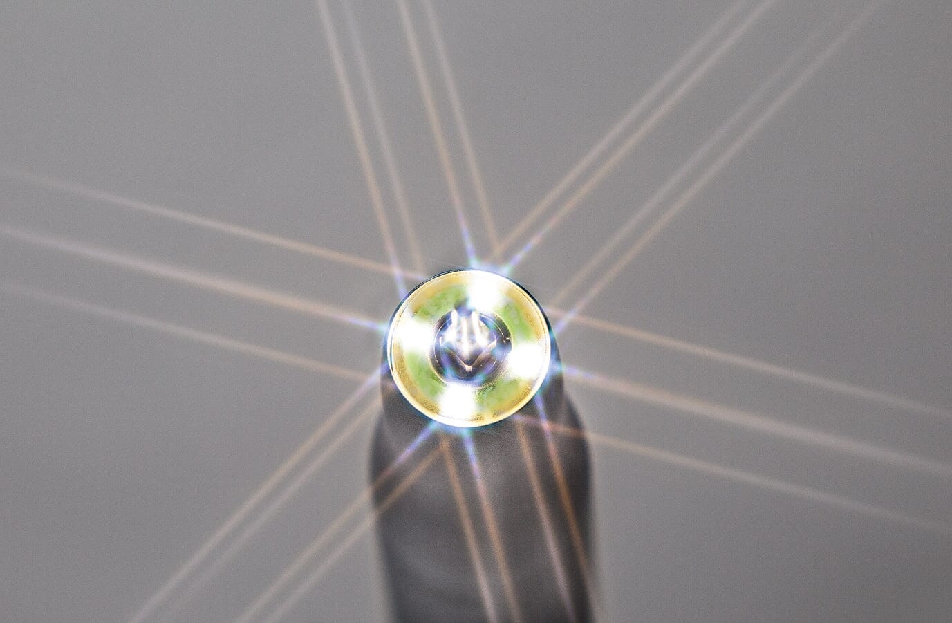 Close-up of a shiny screw head reflecting light in star-like flares, evoking the precision of ultrasonic bone surgery with the W&H Piezomed SA-320 Handpiece with Cable, set against a plain gray background.