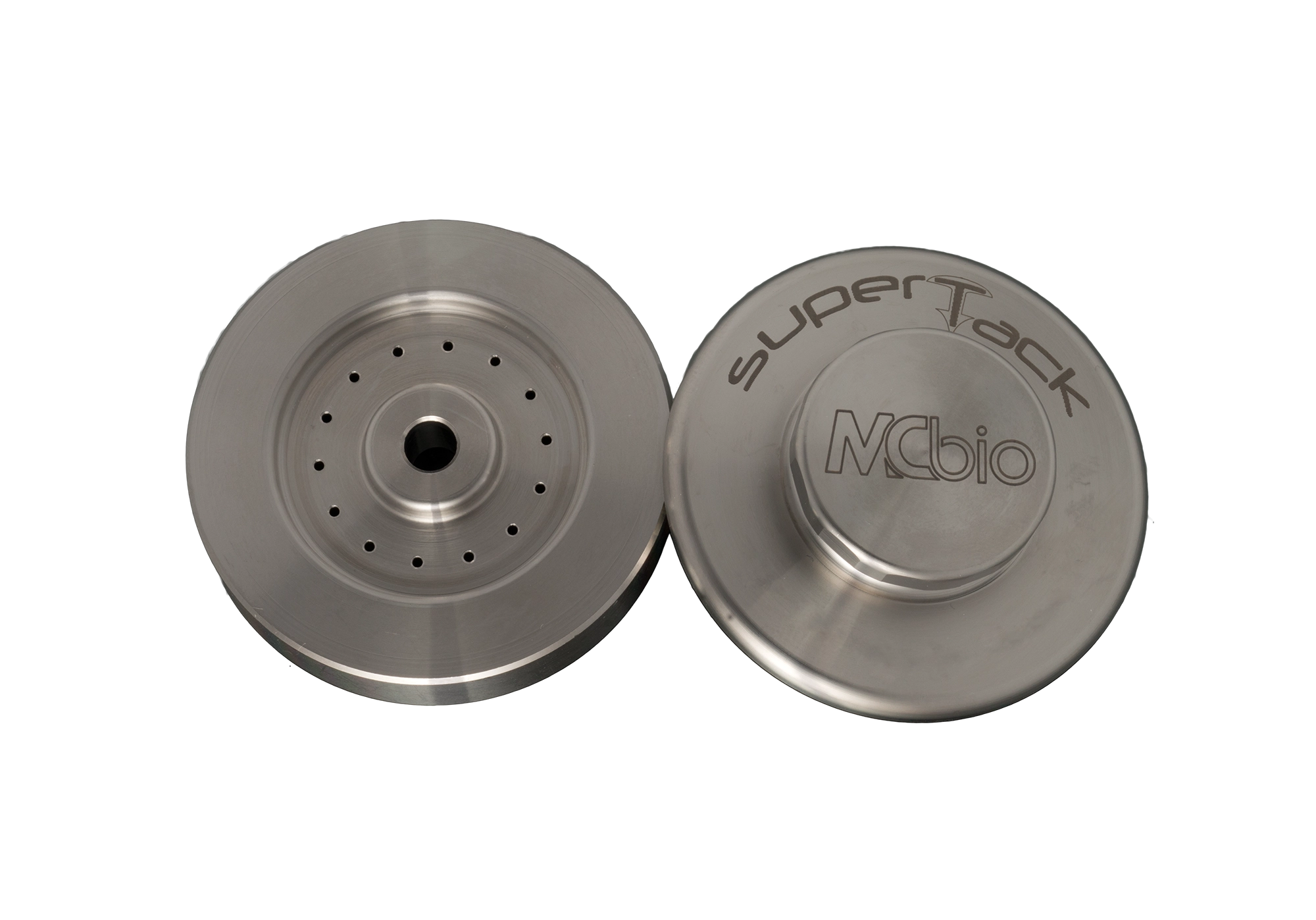 Two round, metallic components are shown. One has several small holes and a central hole; the other is the SuperTack Organizer – Stainless Steel Tack Holder by McBio, used for holding membrane fixation tacks in GBR procedures.