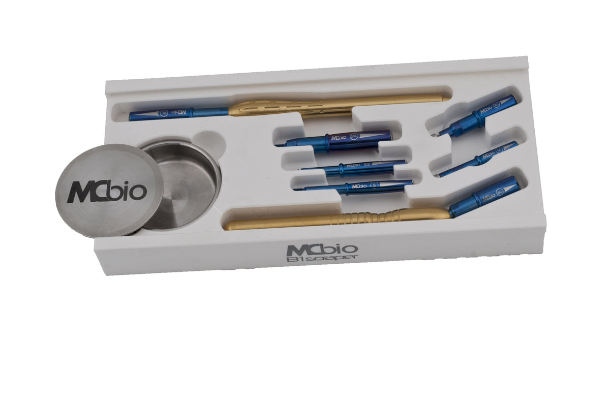 The McBio STS Bone Scraper Master Specialist Kit – Set 7 features blue and gold dental instruments, including a B1 bone scraper and two metal McBio containers, all neatly organized in a white tray with separate slots.